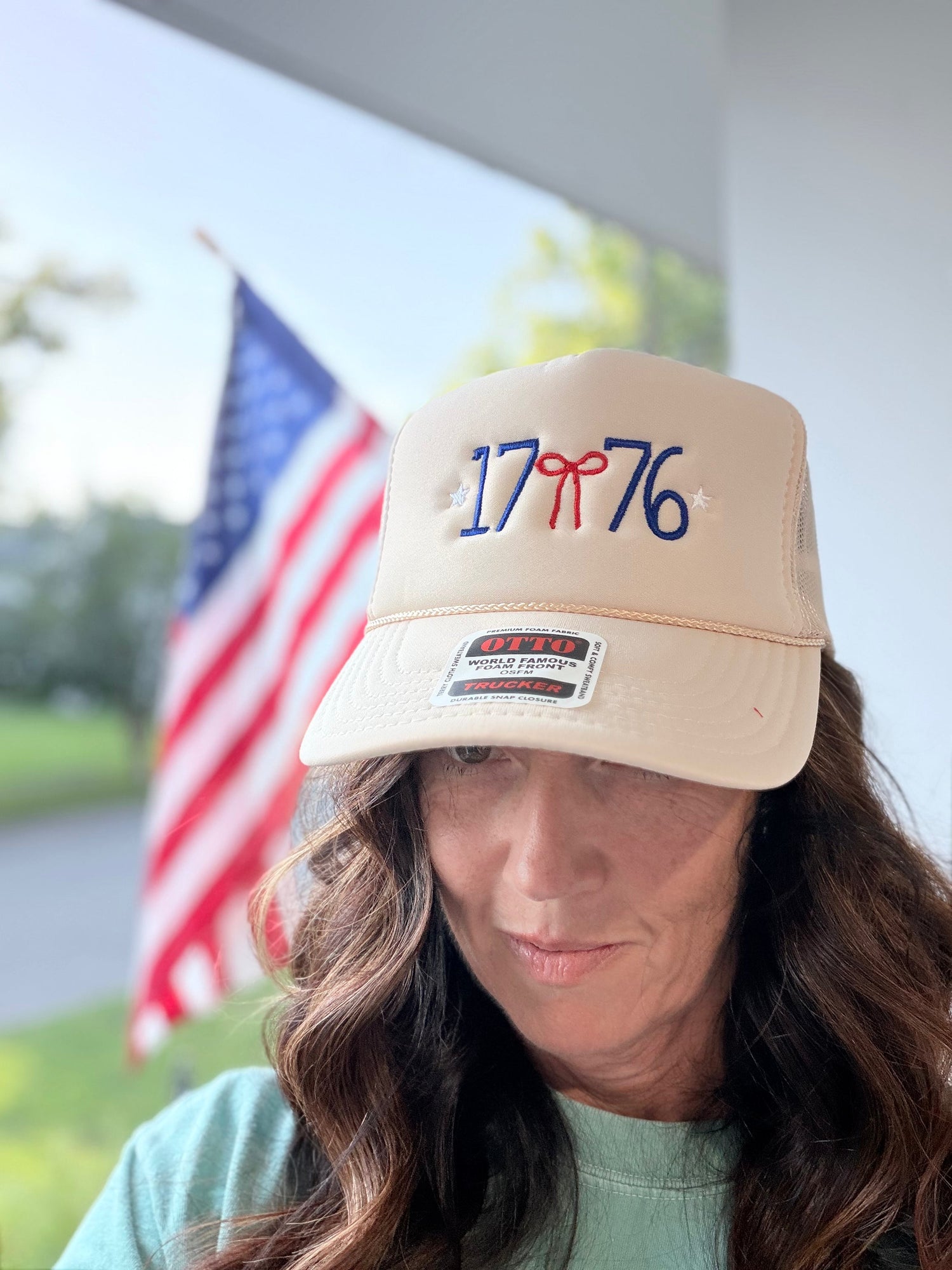 Overhead angle of red and white 1776 embroidered trucker hat showing foam front panel with bow detail and mesh back snap closure